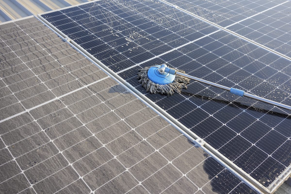 Man using a mop and water to clean the solar panels that are dirty with dust and birds' droppings to improve the efficiency of solar energy storage.